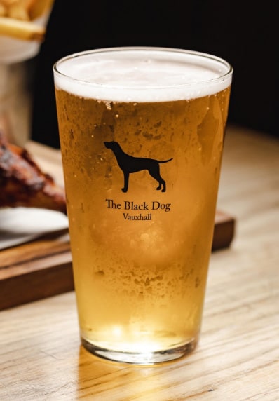 pint glass bearing The Black Dog pub logo, filled with lager